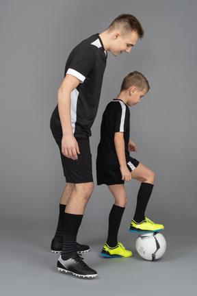 De cuerpo entero de un joven entrenando a un niño pequeño cómo jugar fooyball