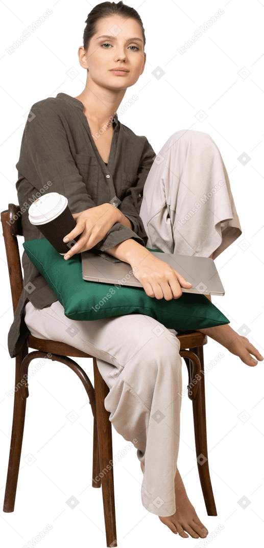 Three-quarter view of a young woman sitting on a chair and holding her laptop & touching coffee cup