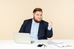 Trabalhador de escritório com excesso de peso jovem insatisfeito sentado à mesa e mostrando porra
