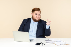 Unzufriedener junger übergewichtiger büroangestellter, der am schreibtisch sitzt und fick zeigt