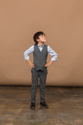Vista frontal de um menino de terno cinza posando com as mãos nos quadris