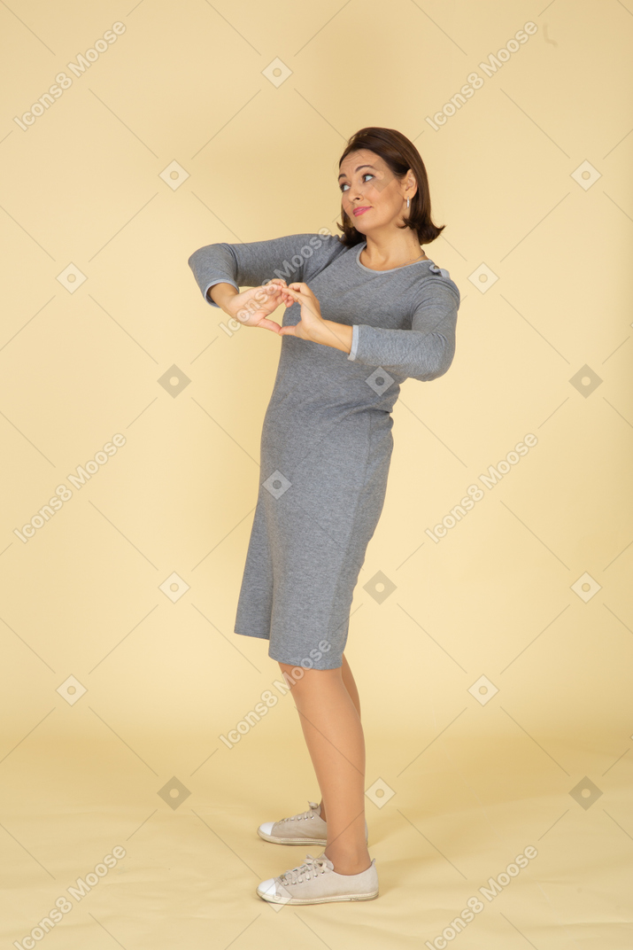 Side view of a woman in grey dress showing heart gesture