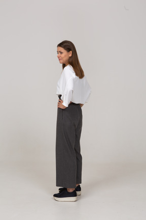 Three-quarter back view of a displeased young lady in office clothing putting hands on hips