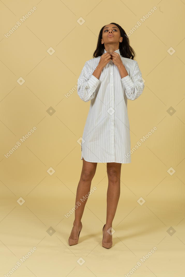 Vista frontal de uma jovem mulher de pele escura em um vestido branco ajustando o colarinho