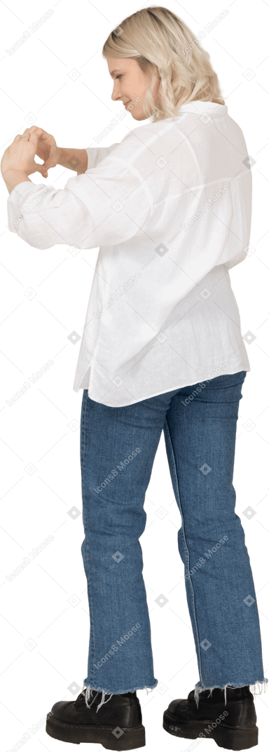 Vista posteriore di tre quarti di una donna bionda in abiti casual che mostra un gesto del cuore