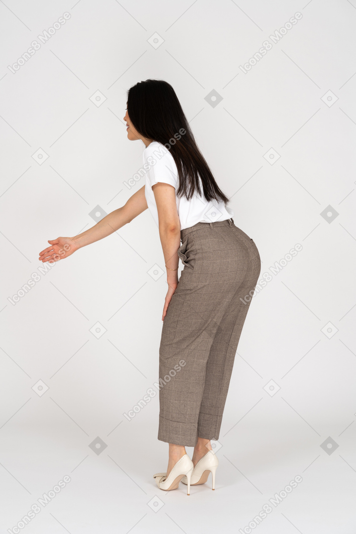 一位年轻的女士，穿着马裤和t恤伸出她的手，弯下腰的侧视图