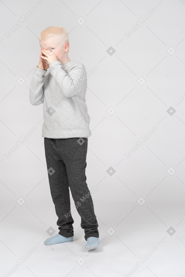 Vista di tre quarti di un ragazzo che si copre la bocca con le mani