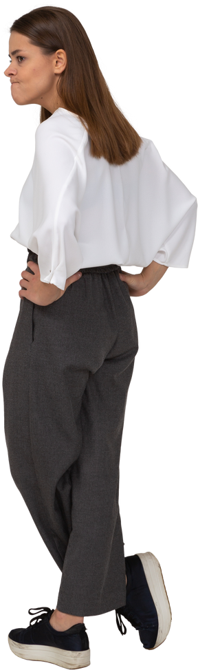 Vista posterior de tres cuartos de una joven disgustada en ropa de oficina poniendo las manos en las caderas