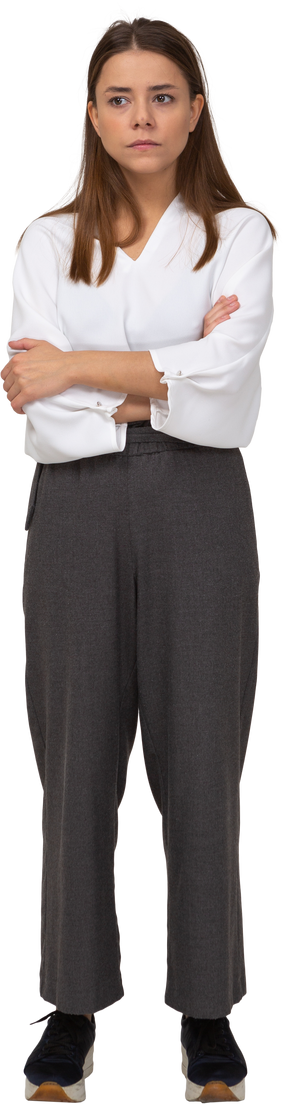 Vista frontal de uma jovem duvidosa em roupas de escritório, cruzando os braços