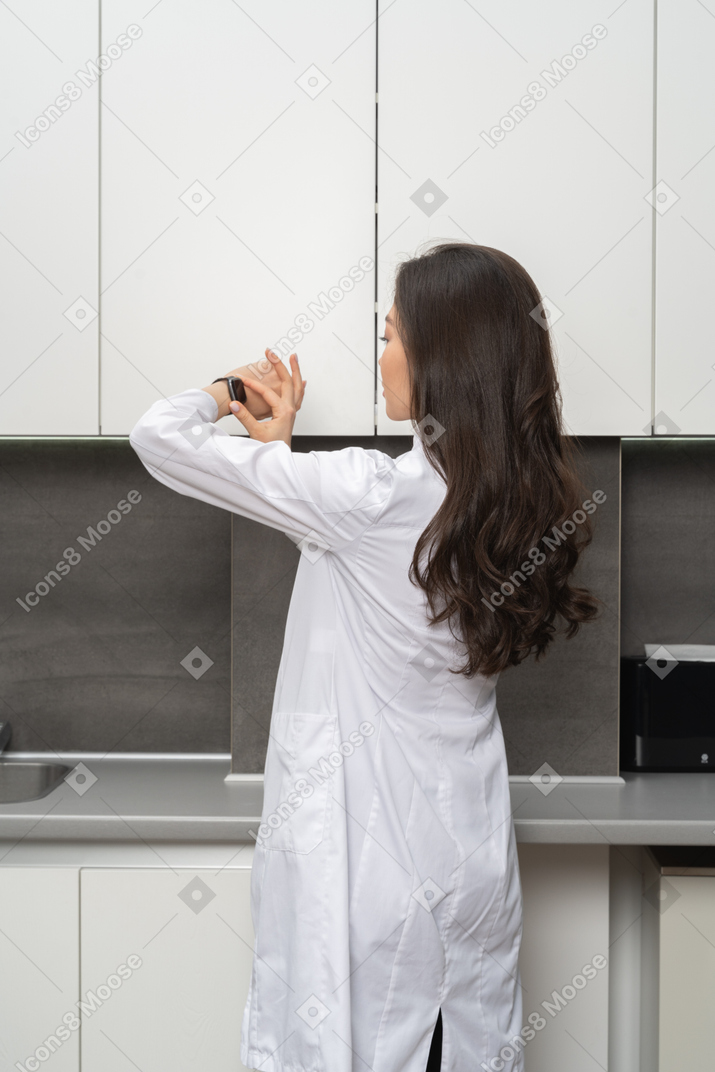 Three-quarter back view of a female doctor putting a timer