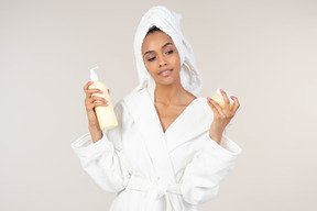 Black woman in white bathrobe and head towel enjoying her skin care routine