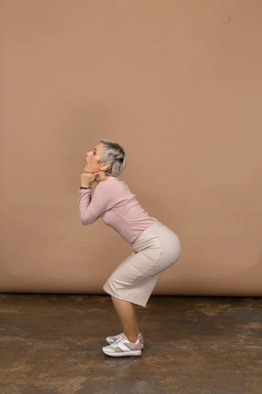 Side view of a woman in casual clothes squatting and making faces