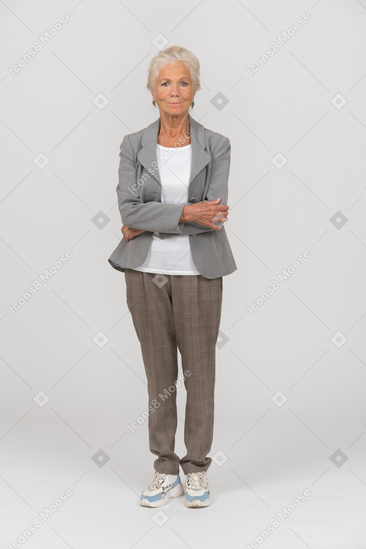 Front view of an old lady in suit standing with crossed arms and looking at camera