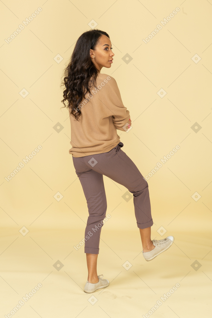 Three-quarter back view of a dark-skinned young female crossing hands