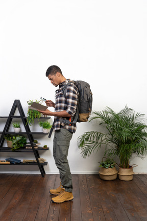 Side view of a tourist with a backpack examining notepad through magnifying glass