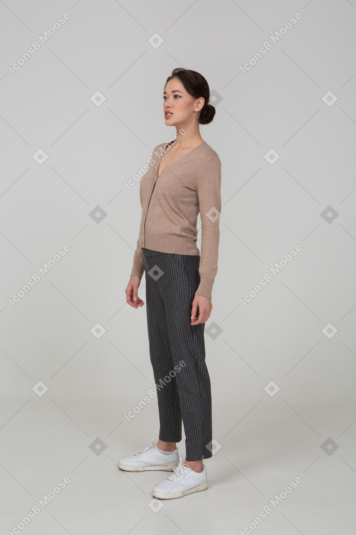 Vista di tre quarti di una giovane donna in piedi ancora in pullover e pantaloni che guarda da parte