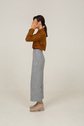 Vista lateral de uma jovem mulher asiática de calça e blusa, levantando as mãos