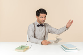 Profesor adulto enojado sentado en la mesa y leyendo un libro