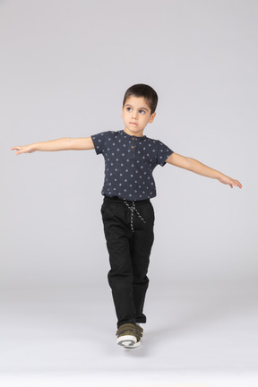Vista frontal de um menino fofo se equilibrando em uma perna e estendendo os braços