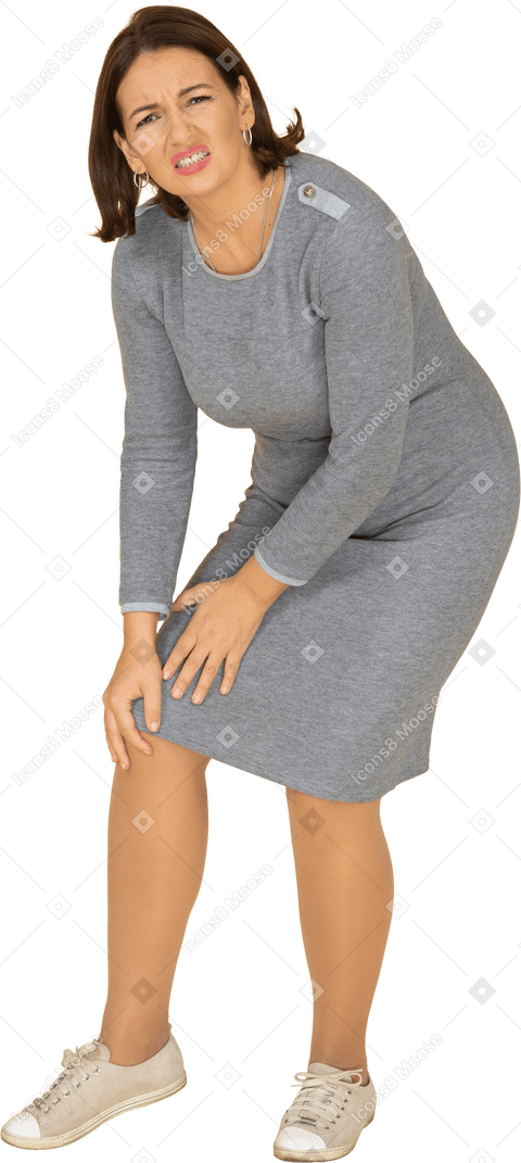 Vista lateral de uma mulher de vestido cinza tocando o joelho