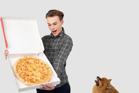 A man holding a pizza box with a dog in the background