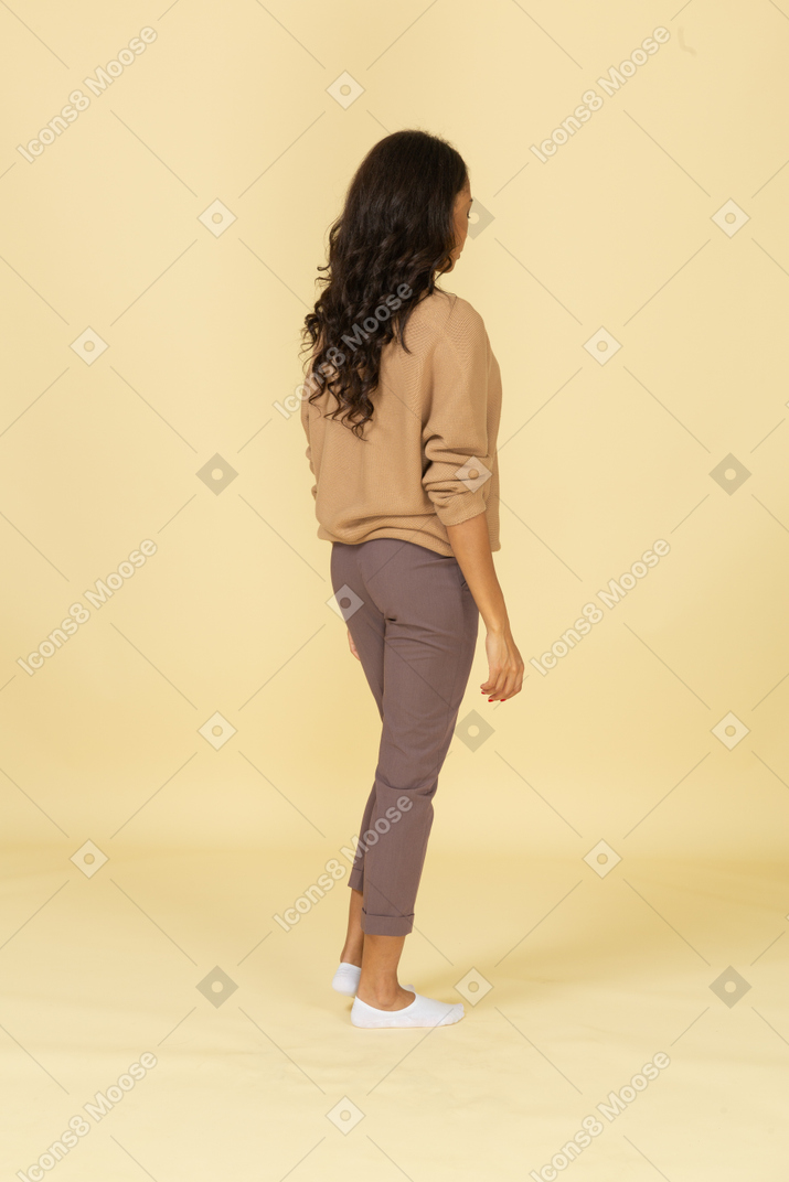 Vista posteriore di tre quarti di una giovane femmina dalla pelle scura in piedi ancora