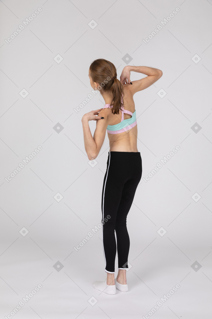 Three-quarter back view of a teen girl in sportswear touching her shoulders and tilting left