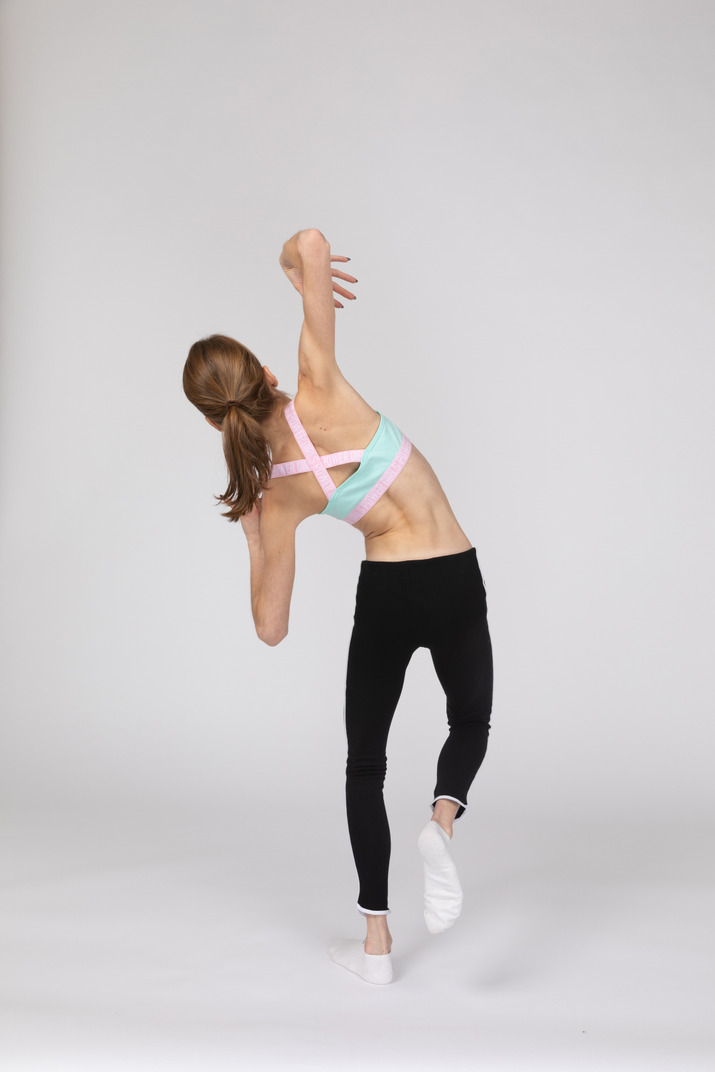 Back view of a teen girl in sportswear tilting her body while raising hand