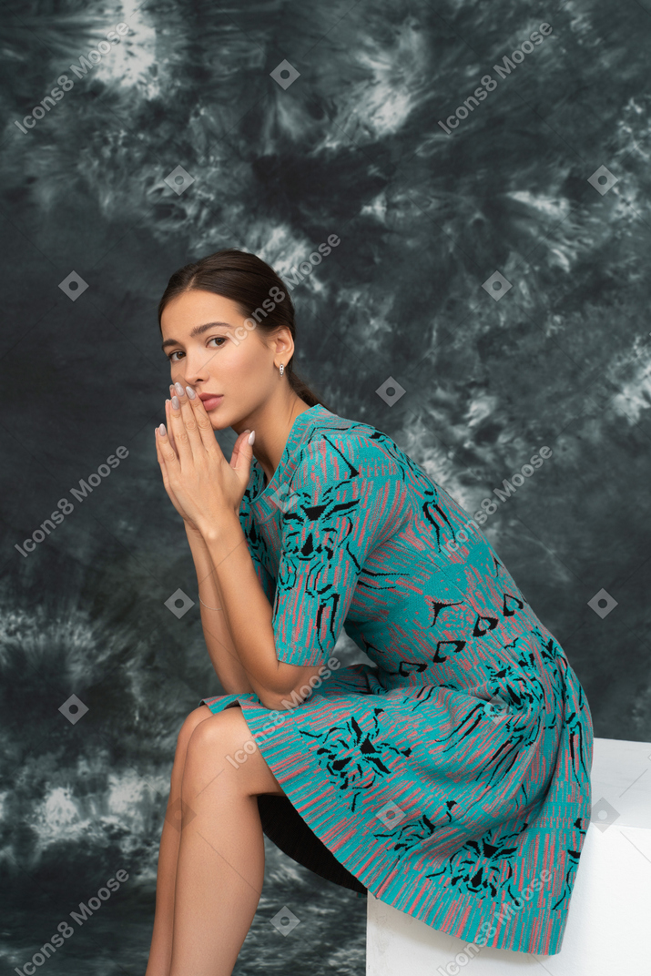 Thoughtful lady in blue dress sits putting hands together