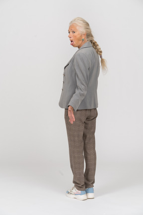 Vista posteriore di una vecchia signora in abito che mostra la lingua