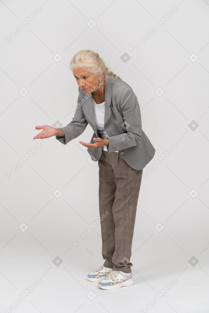 Vista laterale di una vecchia signora in abito che si china e spiega qualcosa