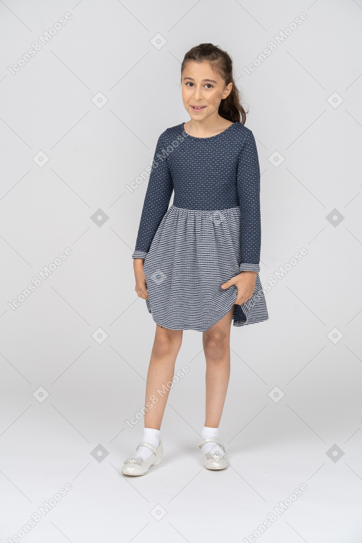Vista frontal de una niña sosteniendo el dobladillo de su falda con una leve sonrisa