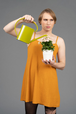 Young transgender person in orange dress watering pot of flowers