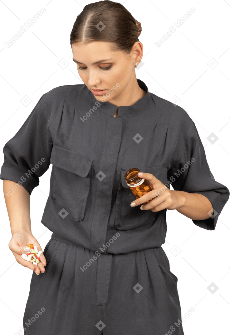 Front view of a young woman in a jumpsuit looking at the pills from a jar
