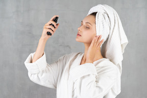 Woman in bathrobe spraying her face