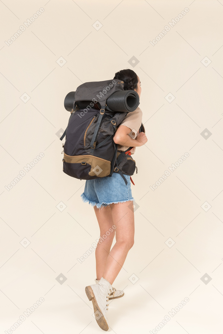 Jovem alpinista feminina carregando mochila pesada e em pé de volta para a câmera