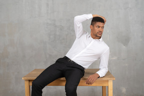 Homme en tenue de bureau assis sur une table et posant
