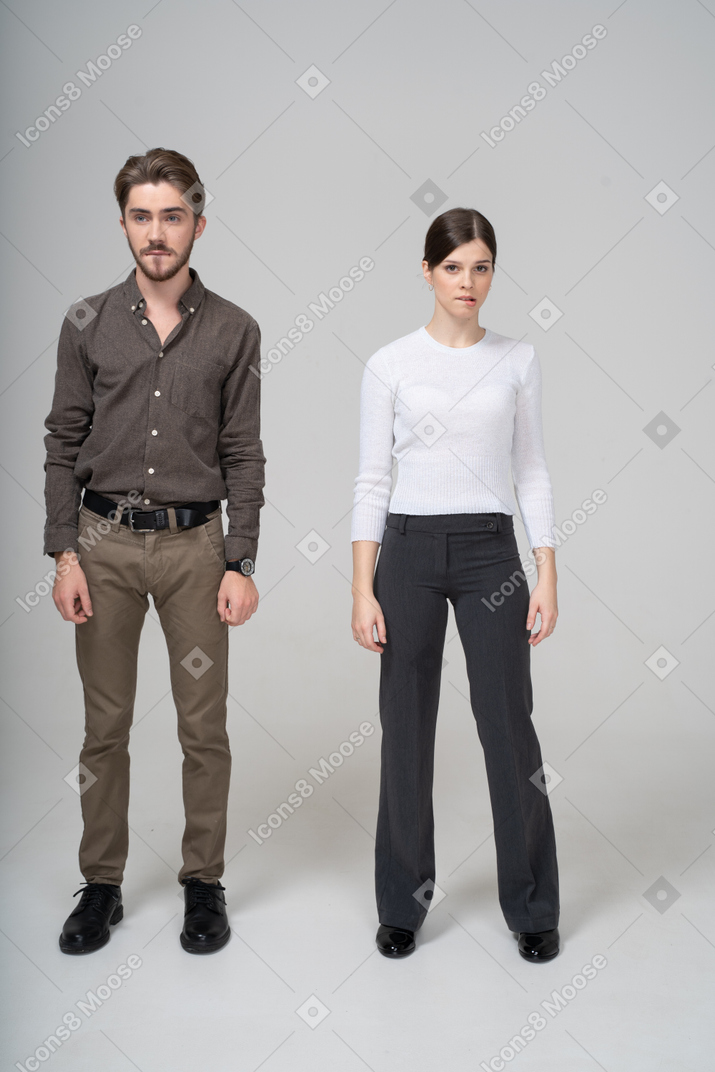 Vista frontal de um jovem casal com roupas de escritório mordendo os lábios