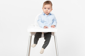 Прелестный ребенок мальчик сидит в стульчике