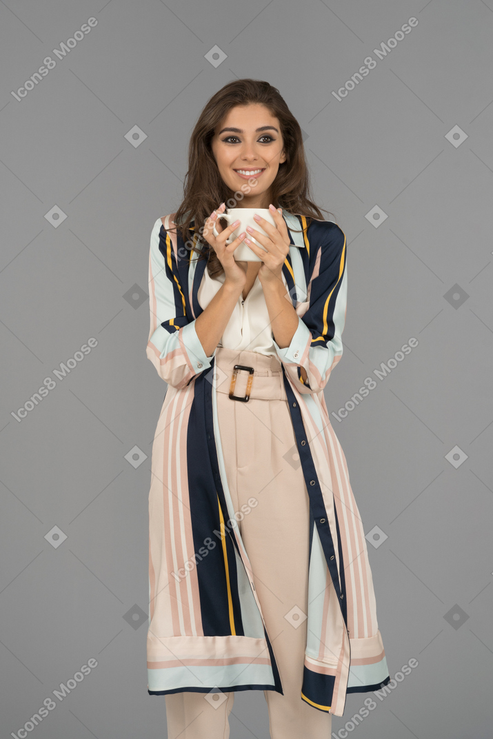 Smiling young woman with a big white cup in hands looking aside