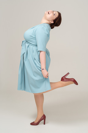 Vista laterale di una donna in abito blu in posa su una gamba sola