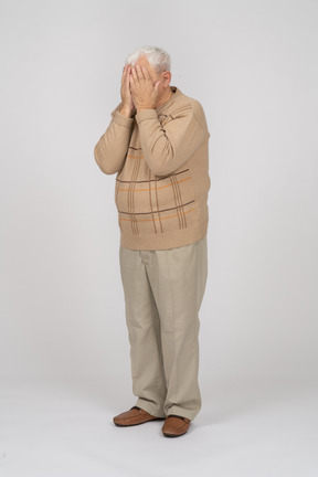 Vista frontal de um velho em roupas casuais, cobrindo o rosto com as mãos