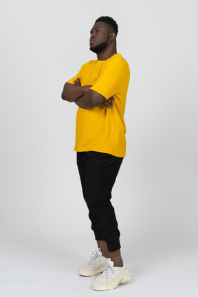 Three-quarter view of a suspicious young dark-skinned man in yellow t-shirt crossing arms