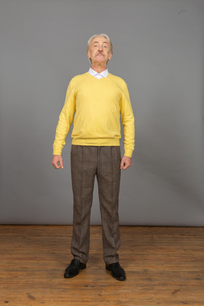 Front view of an old curious man in yellow pullover raising head and looking at camera