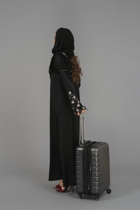 A covered muslim woman standing with a luggage bag