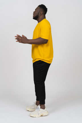 Vista lateral de um jovem chocado de pele escura em uma camiseta amarela levantando as mãos