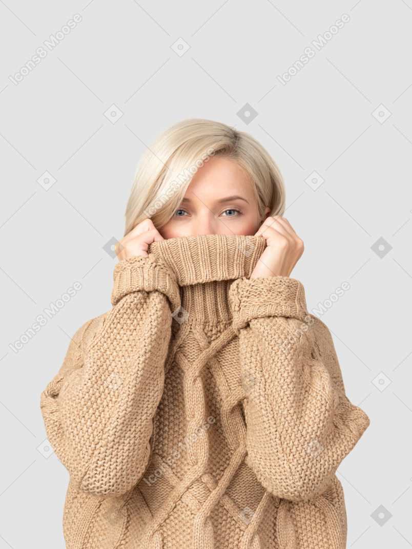 A woman in a cable knit sweater covering her face