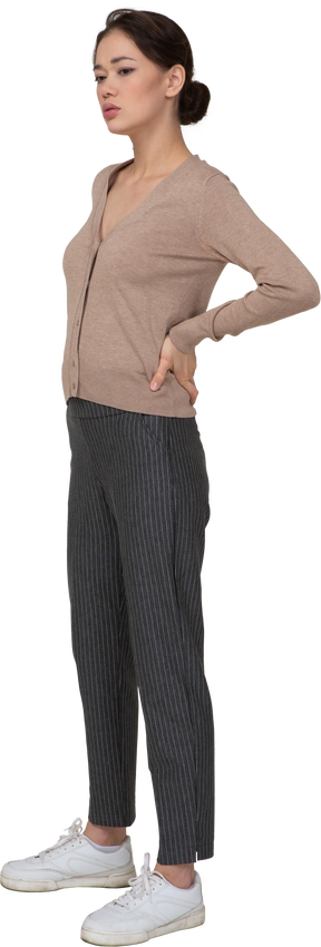 Vista de tres cuartos de una señorita en suéter poniendo las manos en las caderas y los pantalones mirando hacia abajo