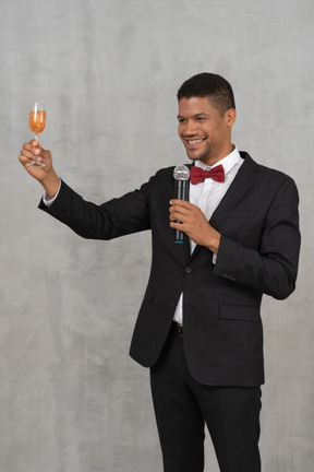 Hombre sonriente con un micrófono levantando su copa