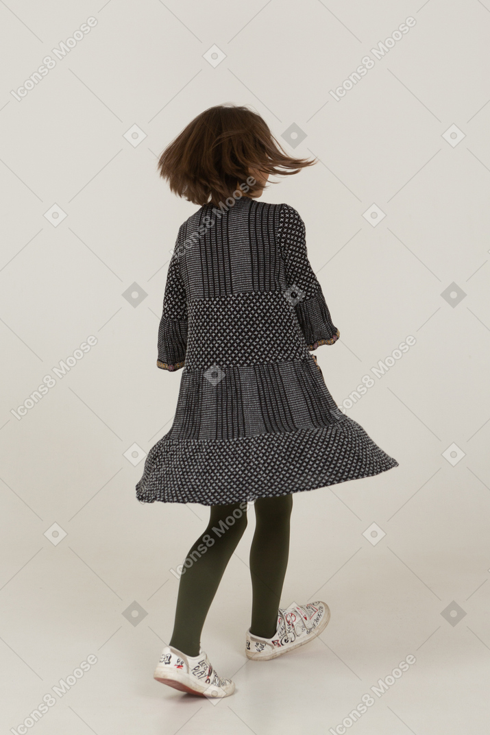 Back view of a dancing little girl with messy hair wearing dress